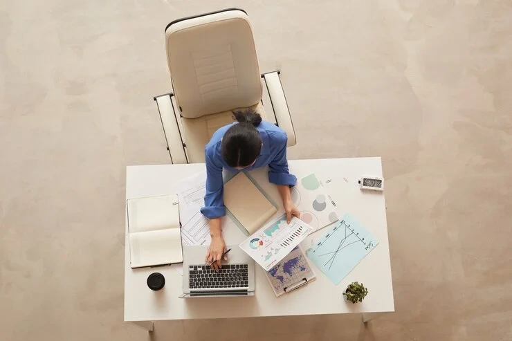 Profesional trabajando en una mesa con gráficos y mapas, destacando la conexión entre la gestión de viajes corporativos y los viáticos y gastos de viaje.