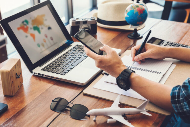 Persona analizando presupuestos y rutas en su laptop y smartphone, representando la renovación de contrato y criterios para elegir una agencia de viajes que permita economizar en 2026.